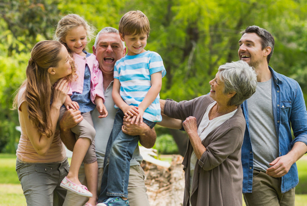 Picture of a large family. The older man is holding a child in each hand. Everyone is smiling.