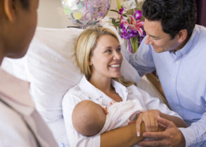 Photo of a smiling mother in a hospital bed holding her baby. The father is also there.