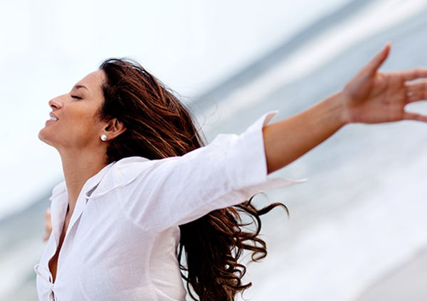 Photo of a woman outside with eyes closed and arms open facing the wind