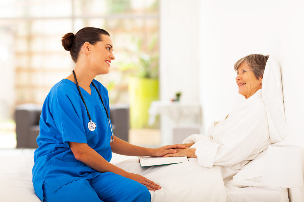 A female doctor sitting with a woman in a hospital bed